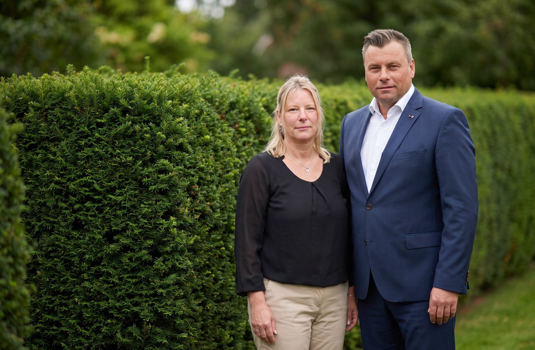 Das Team von Schmidt Bestattungen vor einer Hecke (Bild KI-generiert)